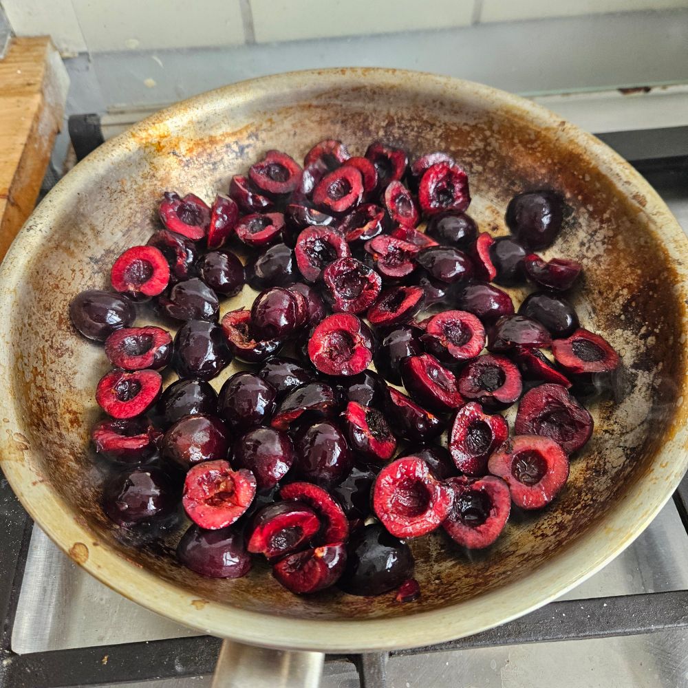 Dark halved cherries getting roasted in a pan that look nasty but I promise it's not