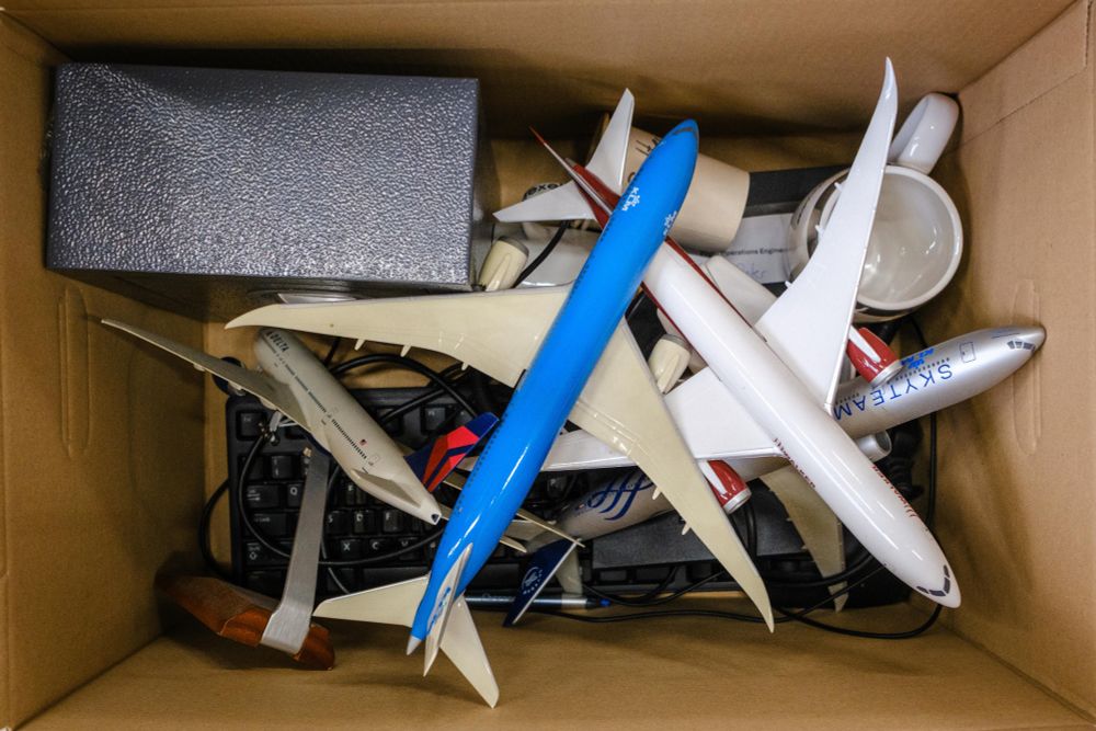 Photograph depicting the inside of a cardboard box containing airplane models and office equipment.