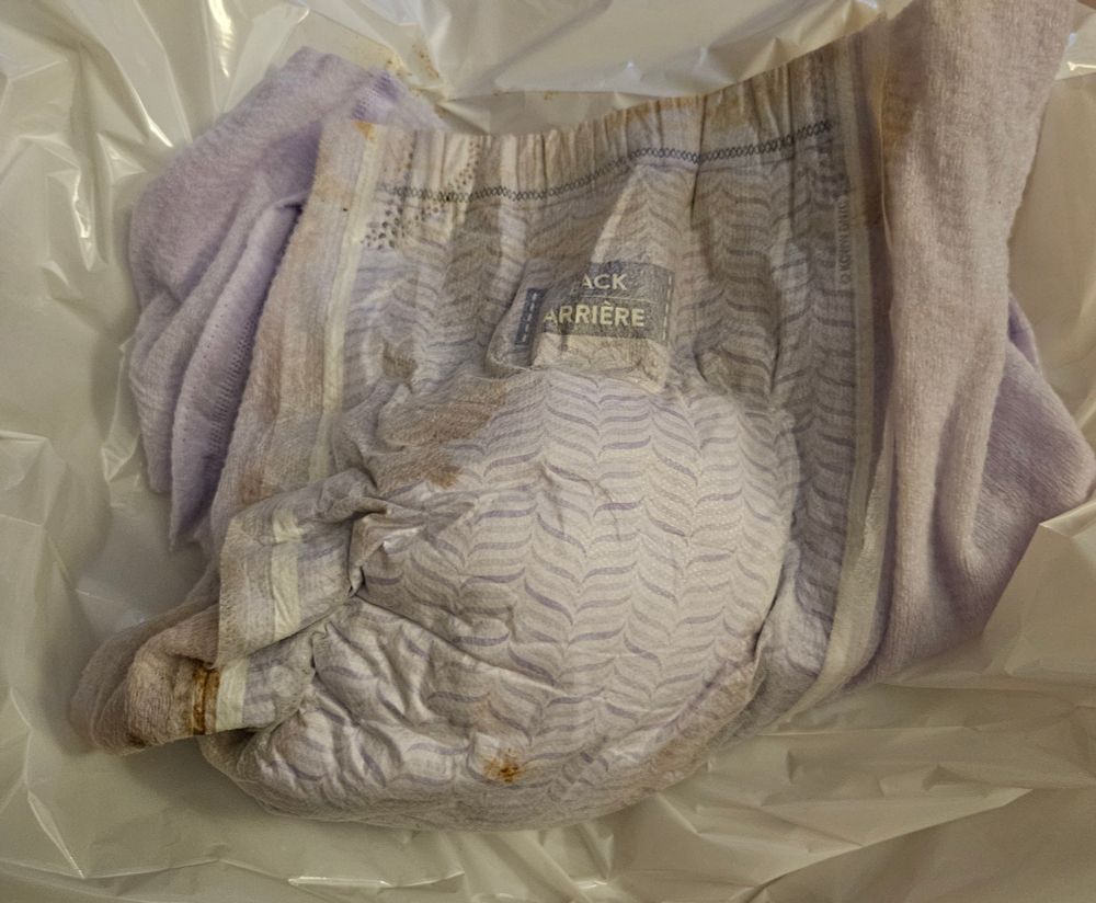 The back of my full purple XXL goodnites laid out on a plastic bag. There are brown stains everywhere