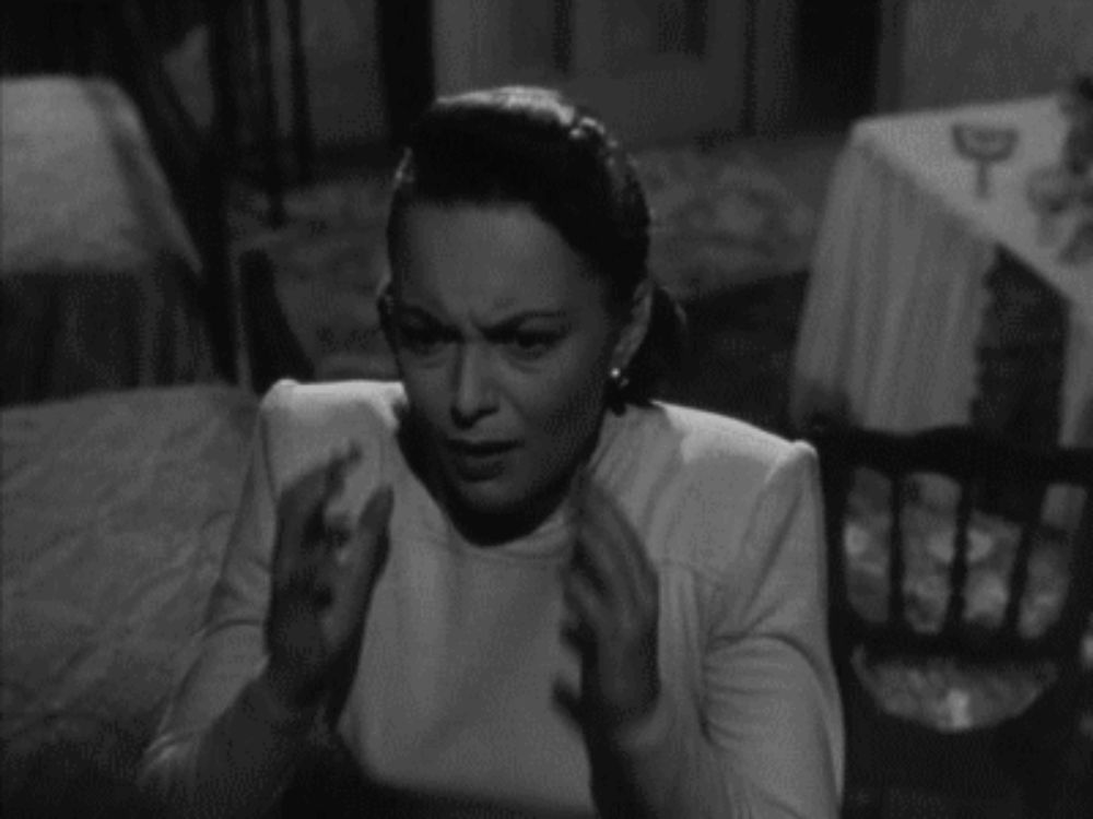 a woman is sitting at a table with her hands on her head in a black and white photo .