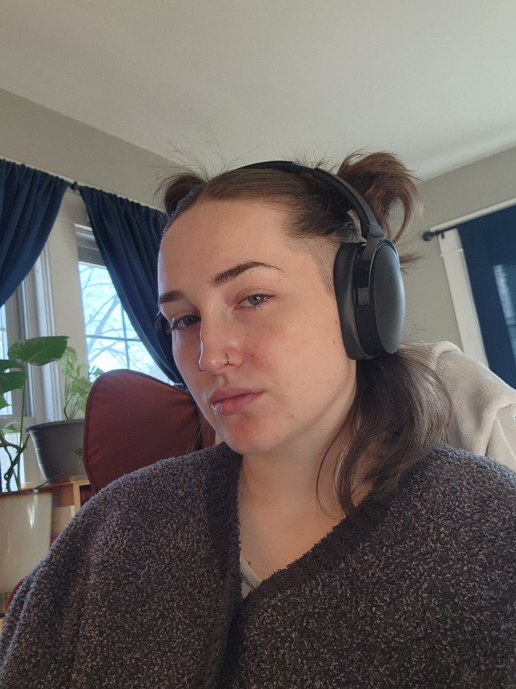Ezra pictured with a half up half down hair style, wearing headphones wearing a gray shaw.