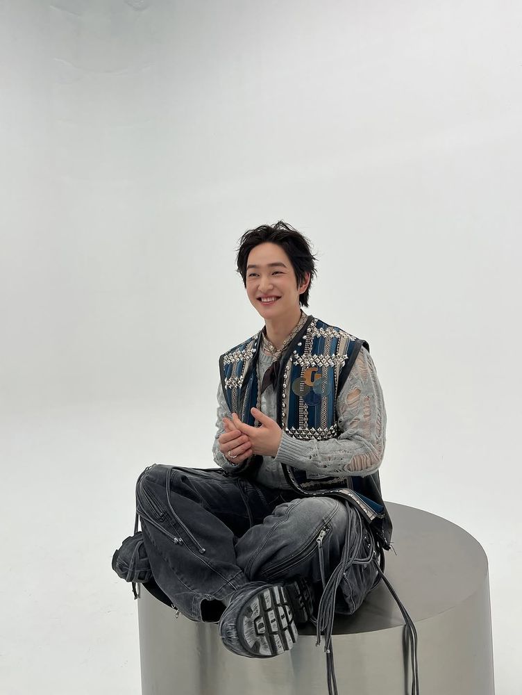 Onew sitting cross-legged and smiling with his hands together