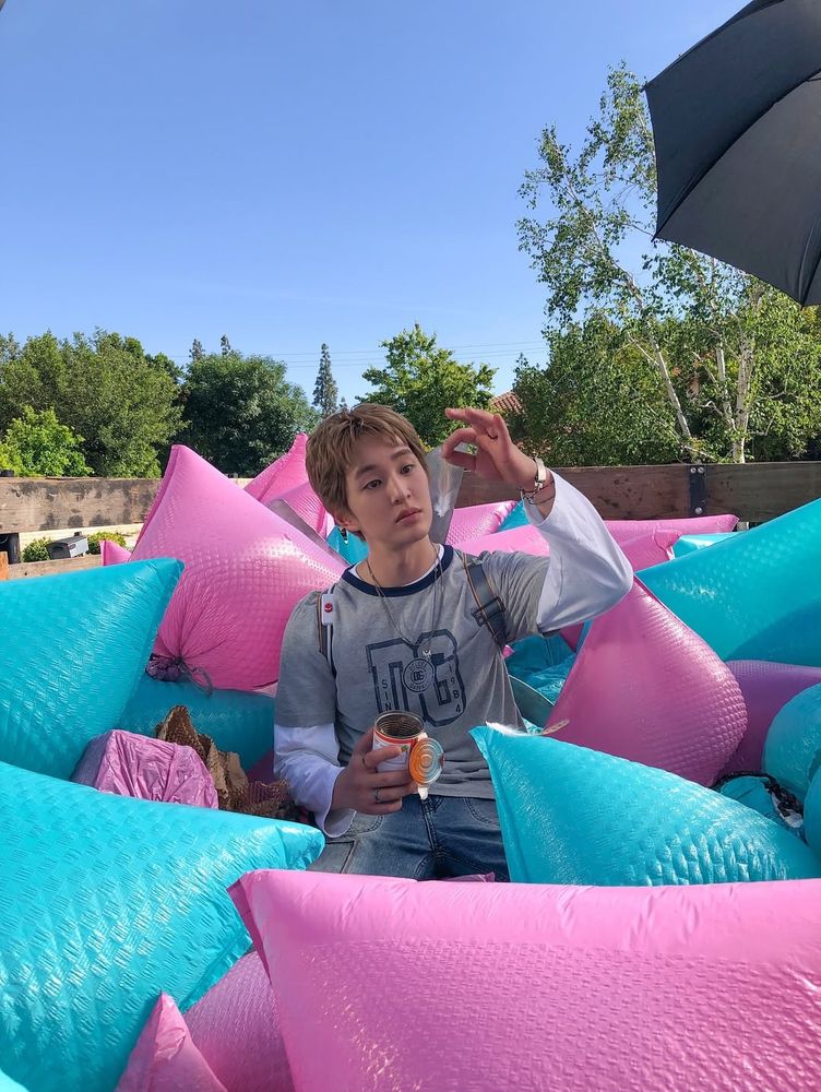 Similar to previous photo but Onew is holding up a feather in his left hand and inspecting it curiously 