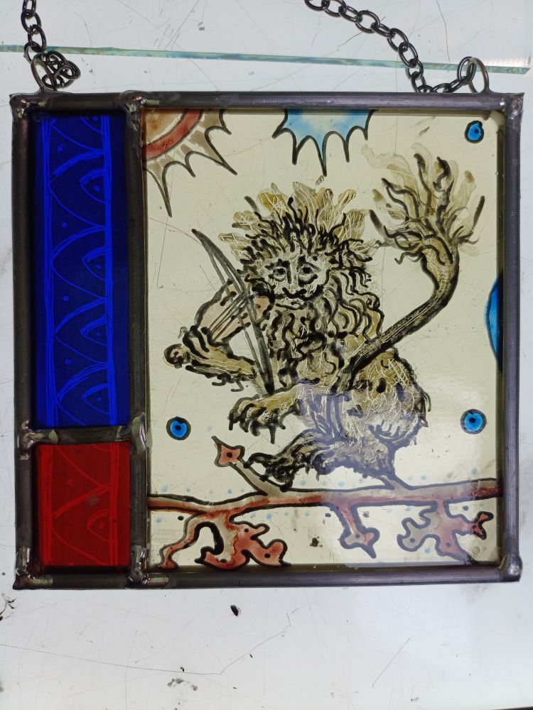 A miserable boss-eyed lion is playing the fiddle whilst balacing on a tree branch. A red and blue border with a pattern runs up the side.