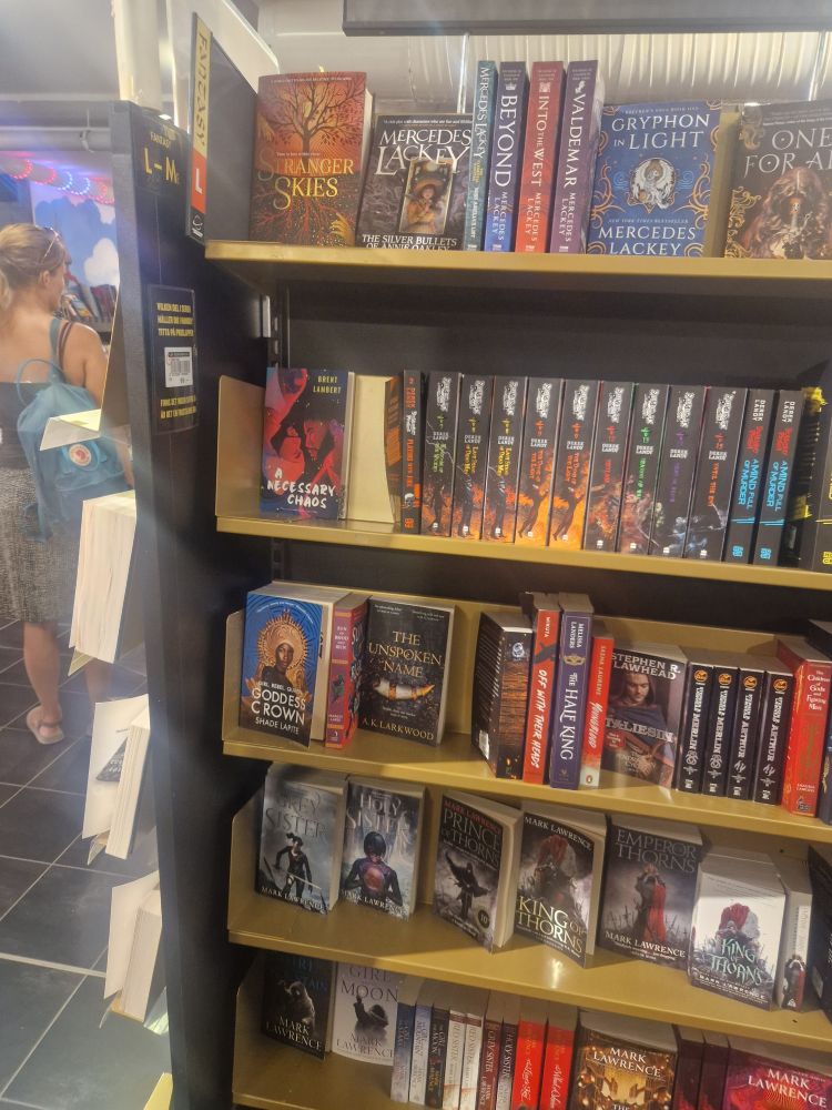 A shelf of fantasy and crossover sff novels with authors whose names start with L. A NECESSARY CHAOS by Brent Lambert is facing out, and we will forgive the shop for also having far, far, far too much Mark Lawrence...