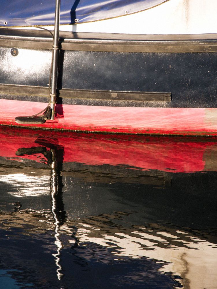 The bottom half of a red, white and blue boat is reflected in the sea at Penryn Harbour in Cornwall. 