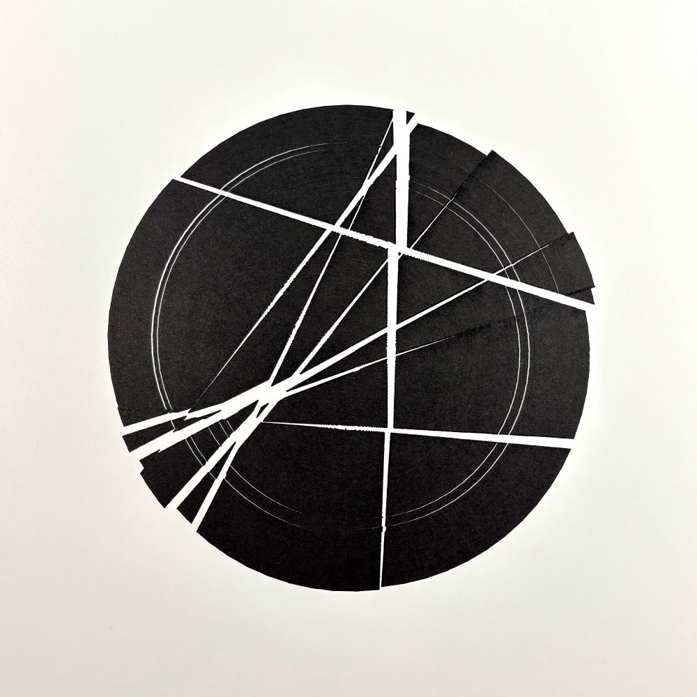 A solid black circle dominates a white background, intersected by several sharp, white diagonal and radial lines that slice through its surface. The circle is fractured into irregular segments, with thin concentric rings etched faintly inside, adding depth.