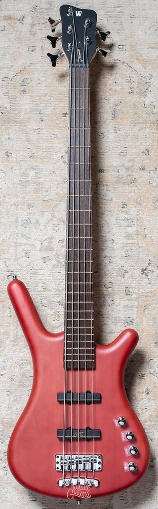 A burgundy finish bass guitar with black fretboard. Edges are all rounded.
