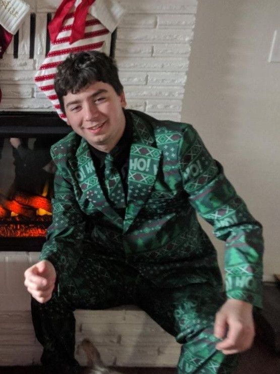 Ashley, pre transition. Short hair, bushy eye brows, ans she's sitting on the stoop of a fireplace in a dorky green x-mas suit.