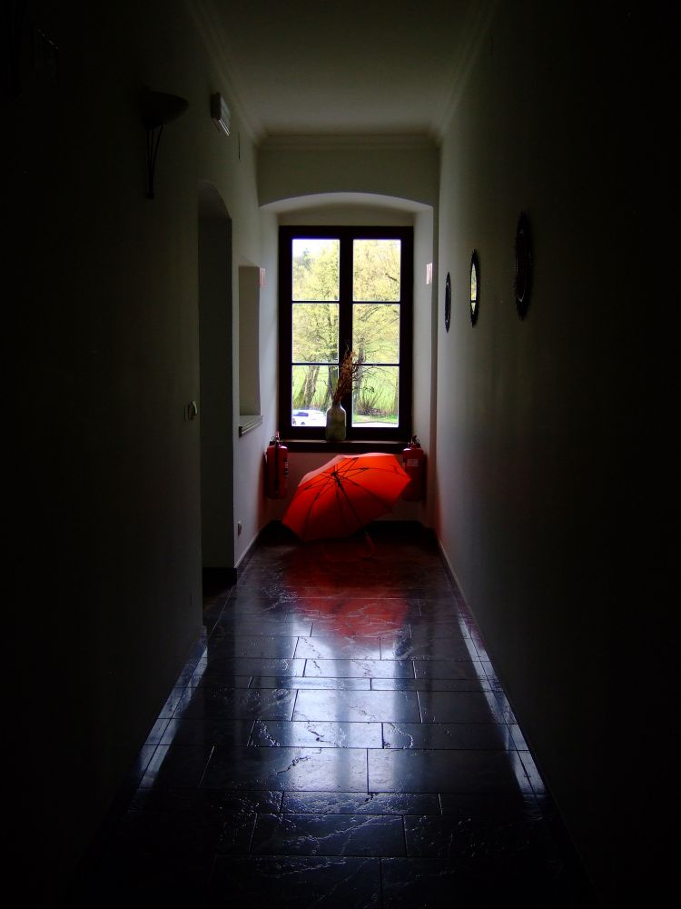 Dark photo of a red umbrella under a window at the end of a hallway.