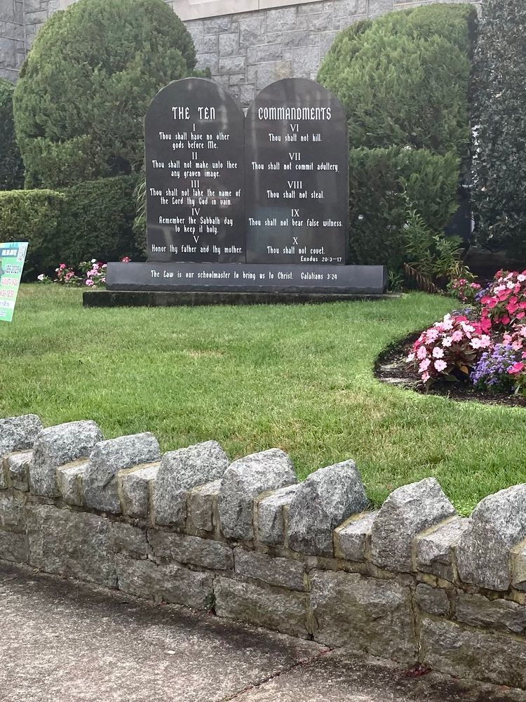 Photo of the ten commandments in front of a church, behind a low rock wall with pointed stones to prevent people from sitting.