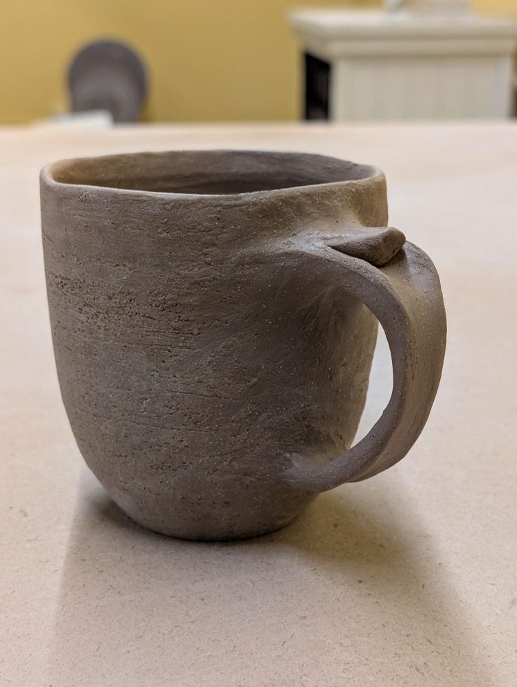 A leather hard speckle clay mug with a pulled handle and a thumb rest 
