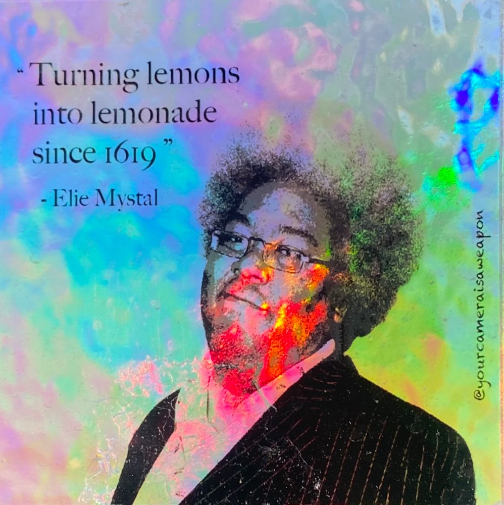 Close-up photo of a silver holographic sticker that was pasted on a light pole on the Upper East Side of Manhattan. A black and white photo of Elie Mystal in a black pinstripe jacket, open-collared white dress shirt, glasses and trademark afro (darker than its current gray). The top of his hair disappears into the psychedelic rainbow background of the hologram. The hologram reflection produces bright orange and yellow on his face and neck as if he’s erupting in flames. He looks straight at you with a deceptively gentle smirk.

Text above and to the left says, “Turning lemons into lemonade since 1619” - Elie Mystal