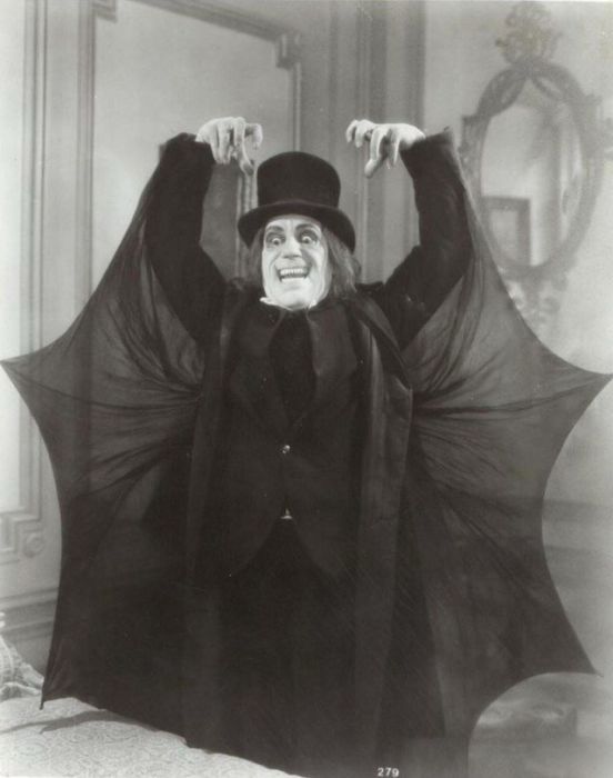 Lon Chaney Sr in London After Midnight (1927)

He stands dressed in black suit, black shirt, black top hat with a maniacal toothy smile.  His arms are up with clawed hands, revealing bat wings sewn into the back of his suit. 