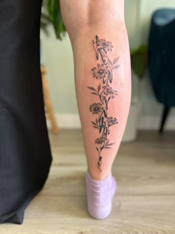 Black calf tattoo that consists of daisies and swirly lines in a bit of an abstract pattern. The tattoo covers the whole back of the lower leg lengthwise.