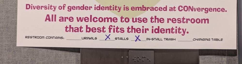 Part of a sign outside a bathroom at a convention reminding attendees that "Diversity of gender identity is embraced at CONvergence. All are welcome to use the restroom that best fits their identity." The bottom of the sign lists the amenities (urinals, stalls, in-stall trash, changing table) in that particular restroom.
