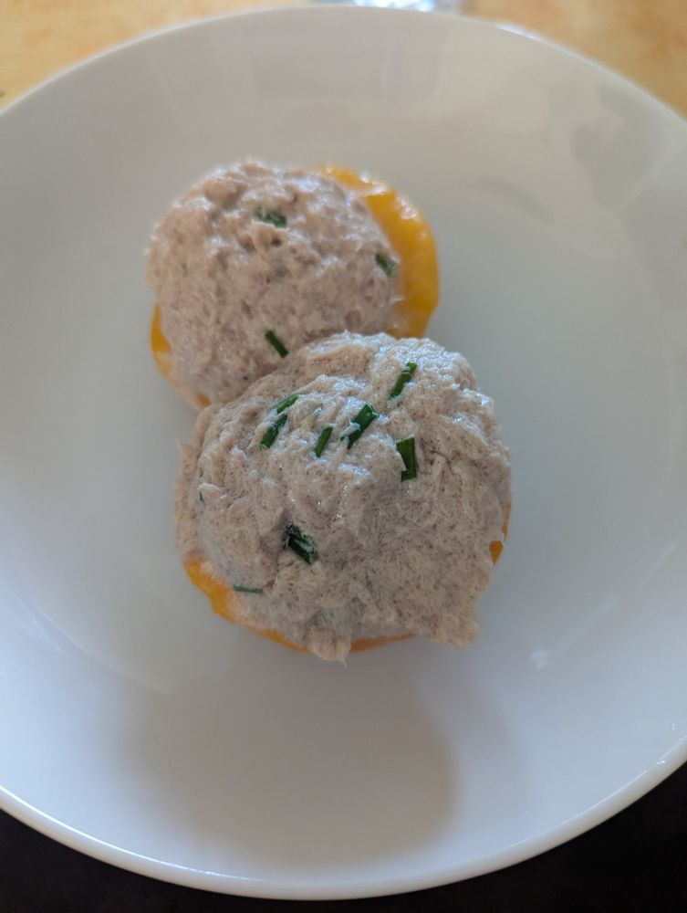 Assiette blanche avec 2 demi-pêches remplies d'un mélange à base de thon, bien rond car fait à la cuillère à glace. 