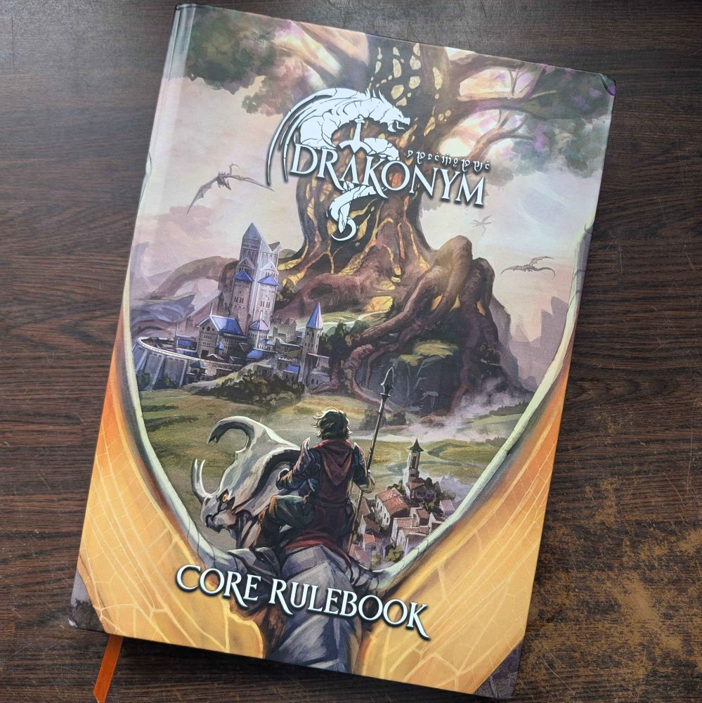 A large tabletop RPG sourcebook. The title is "Drakonym," and it is subtitled "Core Rulebook." On the cover, a dragon rider sits astride their draconic mount, flying towards a walled town at the base of a gigantic tree.