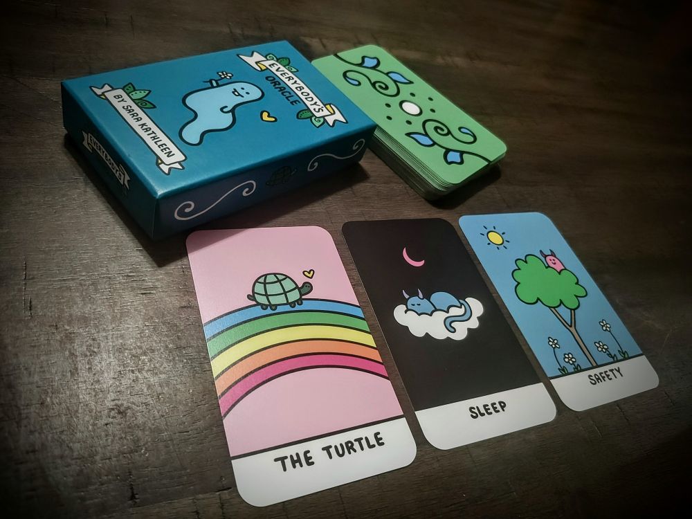 Three brightly colored cards laid across a table with the box and remaining stack of cards