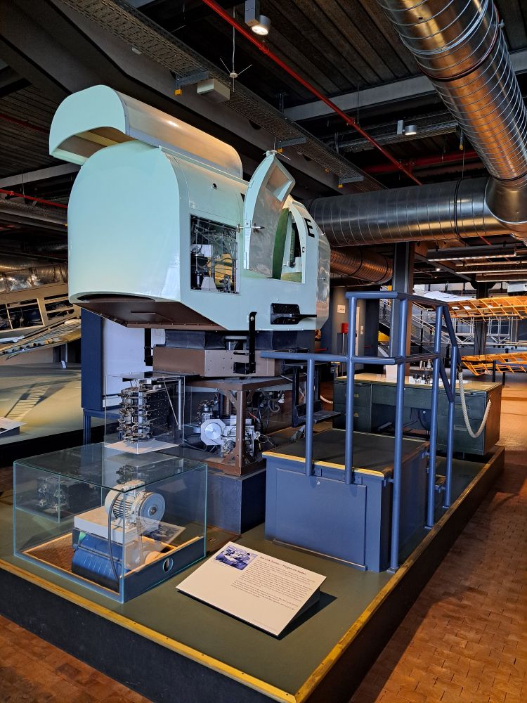 Small pale green cockpit with an open door, mounted on some device that seems to allow banking movements in any direction.