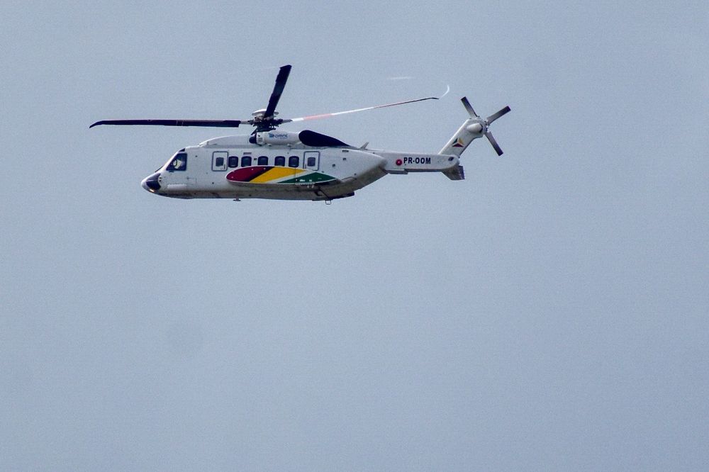 S92 helicopter against the blue sky heading out offshore. Guyana flag colors on the side. (Red yellow and green)