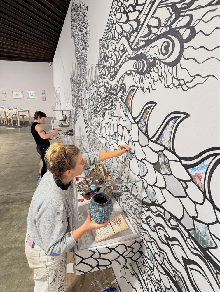 Two people add details to the scales of the large dragon mural created by Ursula Barton. 