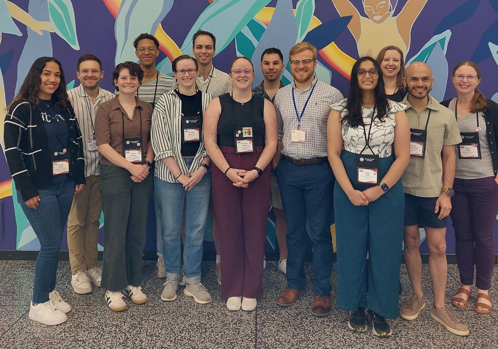Group photo of UNC virologists attending the 2025 American Society for Virology conference in Montreal. They are standing in front of a brightly colored mural, wearing their conference name badges, with bright smiles because of all the virology.