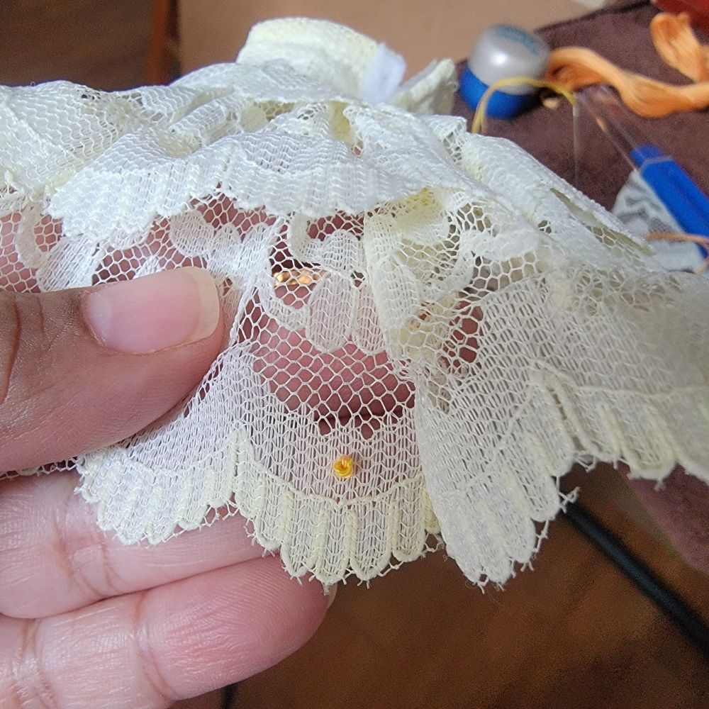 Close up of off white lace dress with pale yellow French knots. 