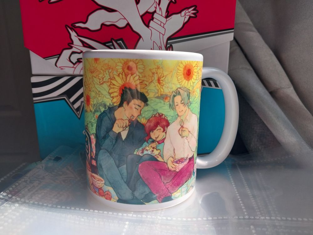 A picture of Periwinkla's Narumitsu family mug. It shows Phoenix Wright, Miles Edgeworth, and Trucy Wright having an adorable picnic together.