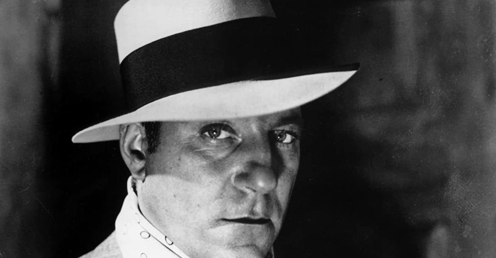 A close up of Jean Gabin from the film Pepe le Moko. He is wearing a white brimmed hat with a black band. 