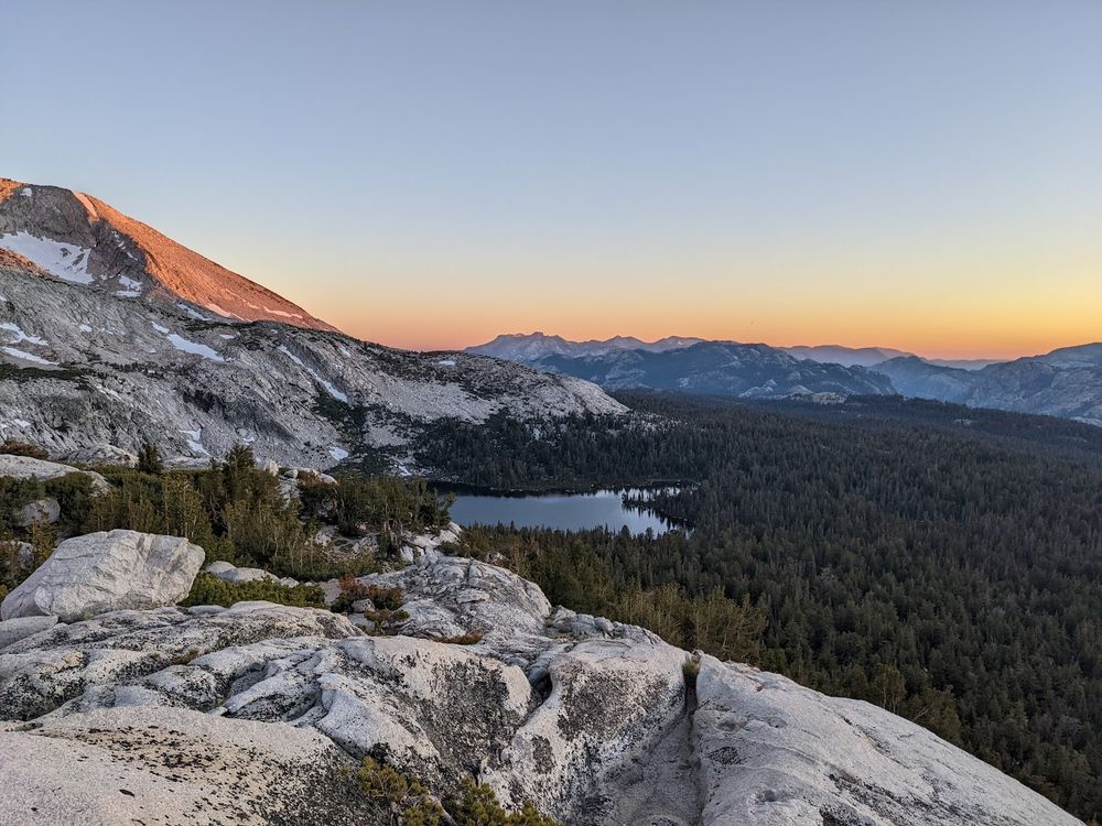 Granodiorite weathered peaks at sunset overlooking a glacial lake in a dense coniferous forest