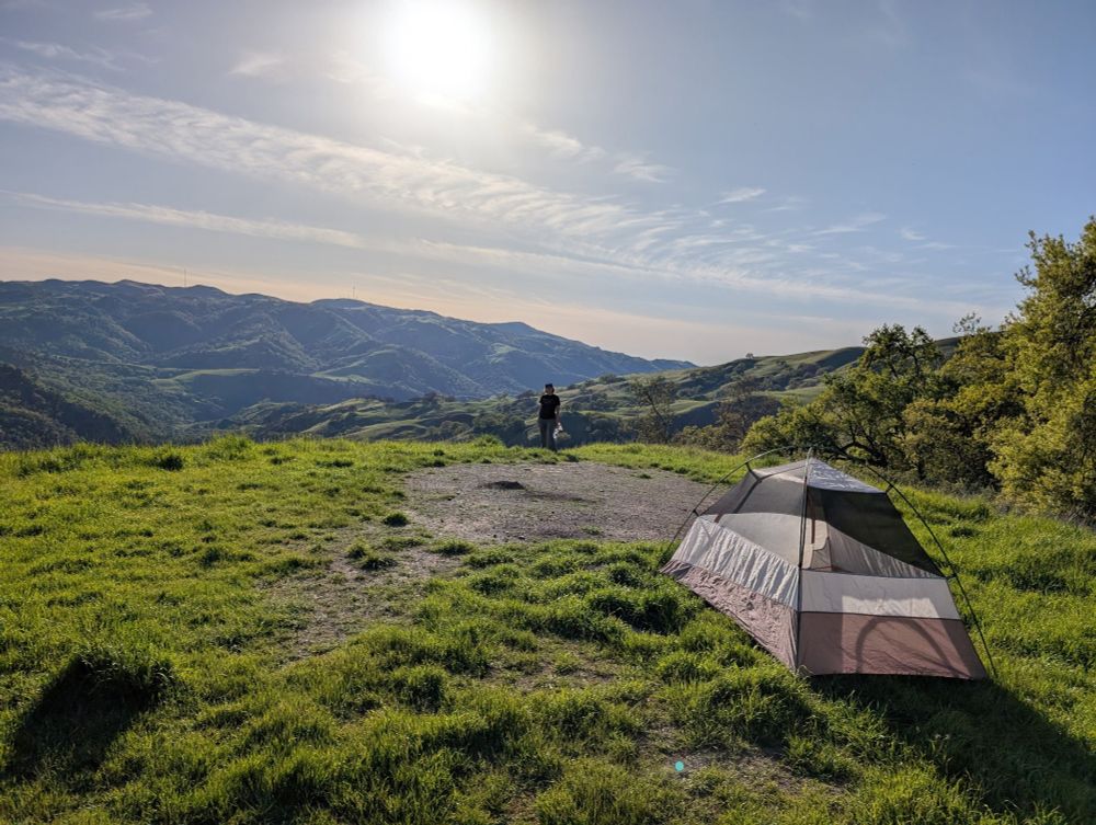 Tent on a flat campsite overlooking lush green hills