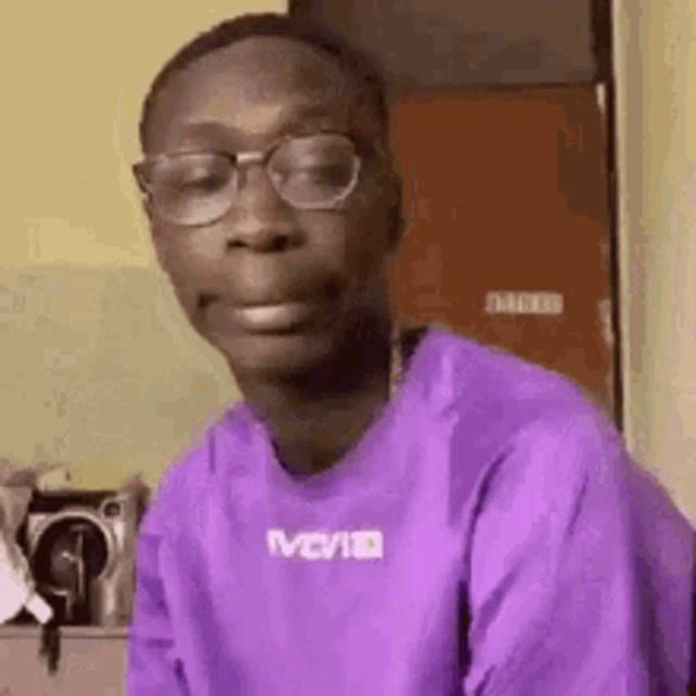 a young man wearing glasses and a purple shirt is making a face .