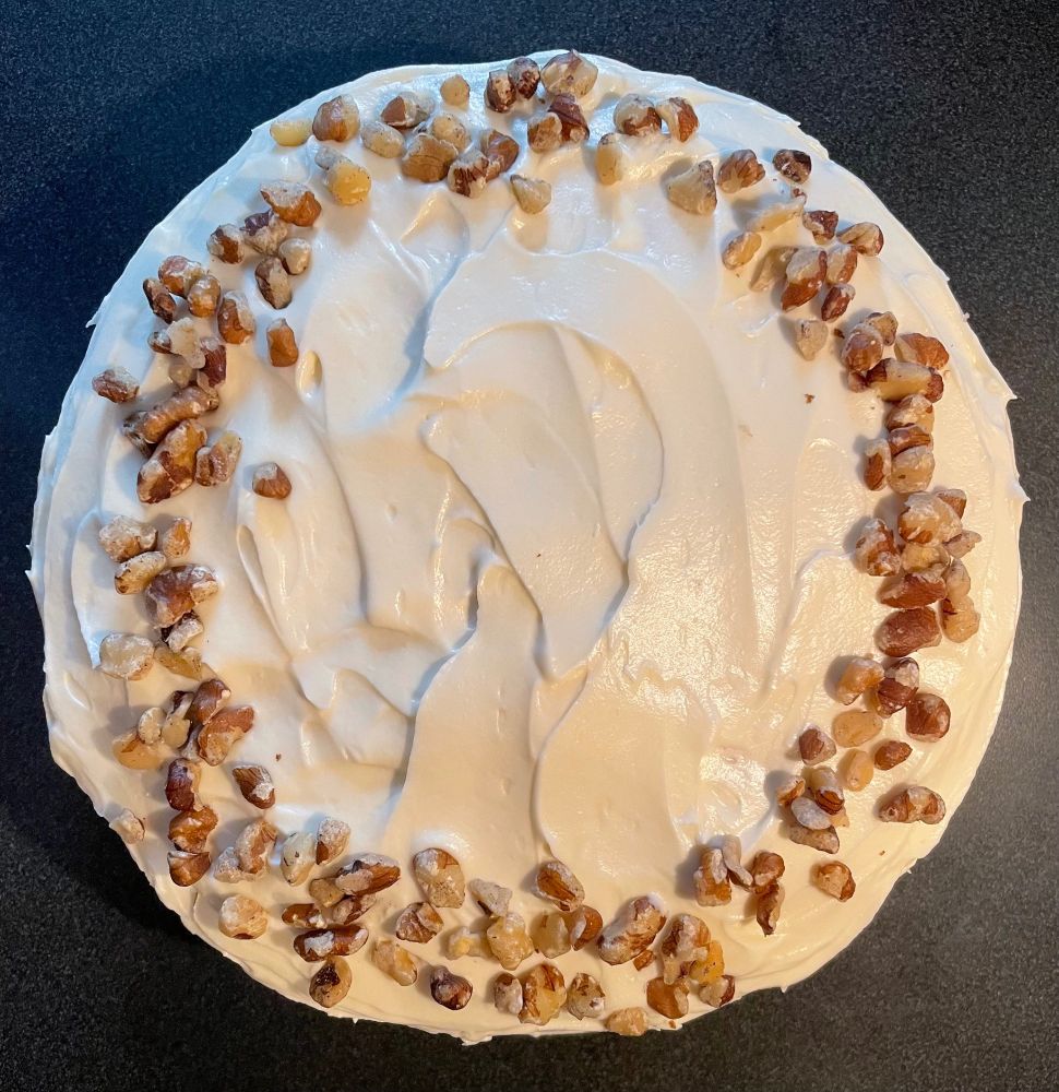 A top-down view of the frosted cake with a ring of chopped black walnuts around the edge