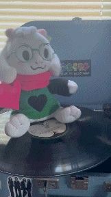 a stuffed animal with glasses and a scarf is sitting on top of a record player