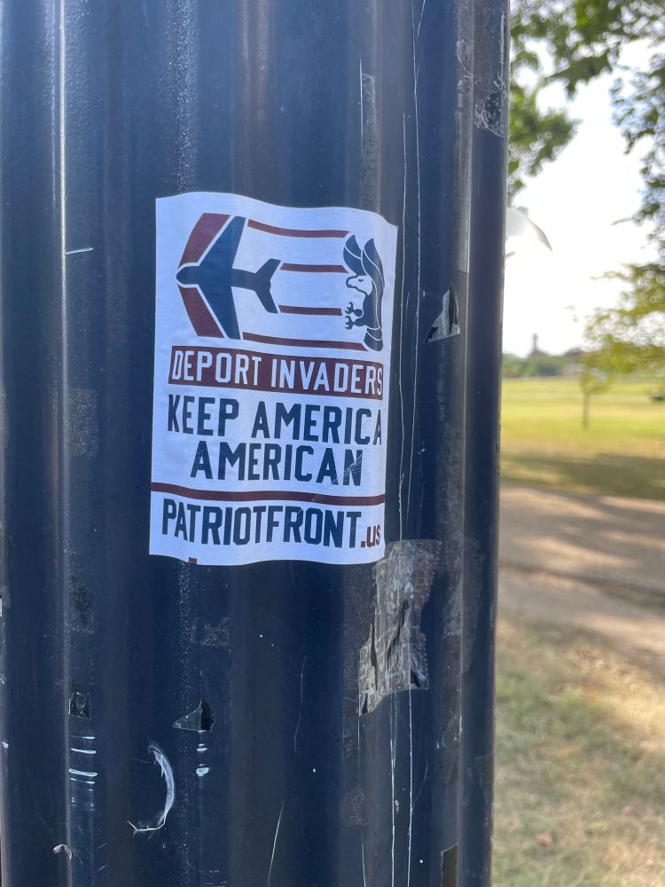 Sticker on lamppost. Image: plane flying away from bald eagle. Text: “Deport invaders. Keep America American”