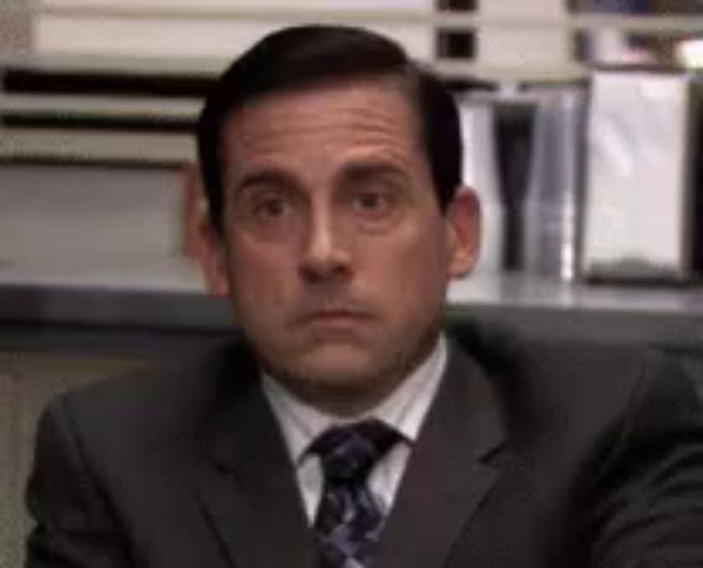 a man in a suit and tie is sitting at a desk and looking at the camera .