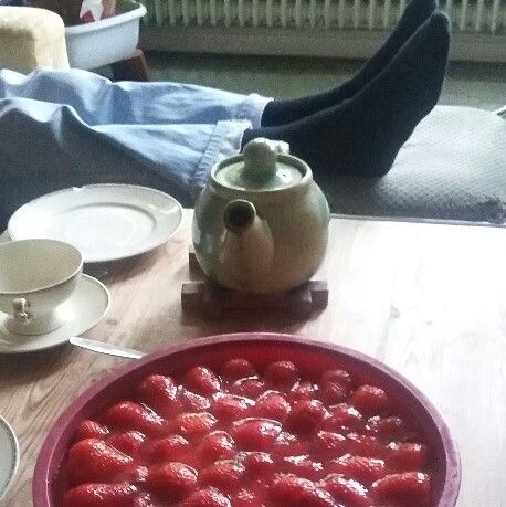 Tisch mit Erdbeertorte, Im Hintergrund Füße auf einem Stuhl