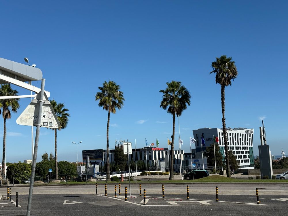 A wide shot of a modern cityscape, featuring palm trees, a hotel, and a bright blue sky. The combination of architecture, signage, and natural elements gives a sense of a sunny, metropolitan environment.