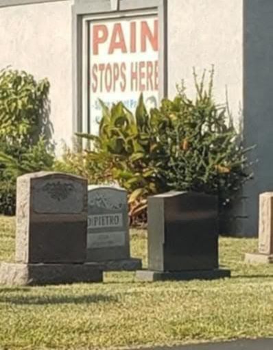 A window with a sign that says "PAIN STOPS HERE" and in front of the building there are cemetery stones