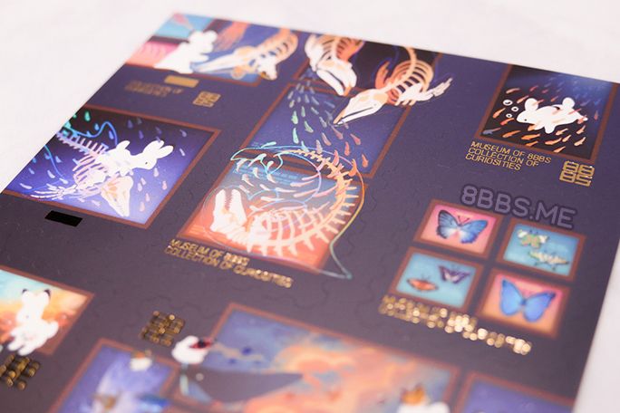 Close-up photo of the upper half of a foiled sticker sheet featuring rabbits and crows in a museum/gallery sort of setting. Light catches on the clear holo foil making it look faintly rainbow.
