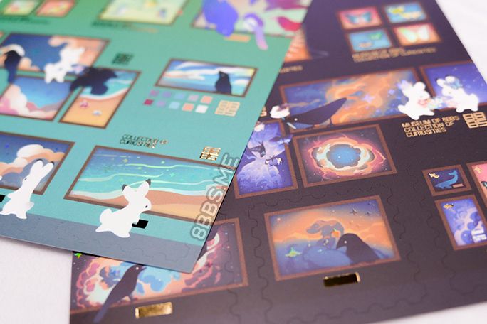 Close-up photo of 2 foiled sticker sheets featuring rabbits and crows in a museum/gallery sort of setting. Light catches on the clear holo foil making it look faintly rainbow.