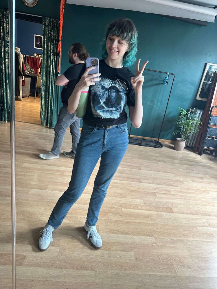 Woman in a “Bella where the hell have you been loca” shirt making a peace sign at a mirror