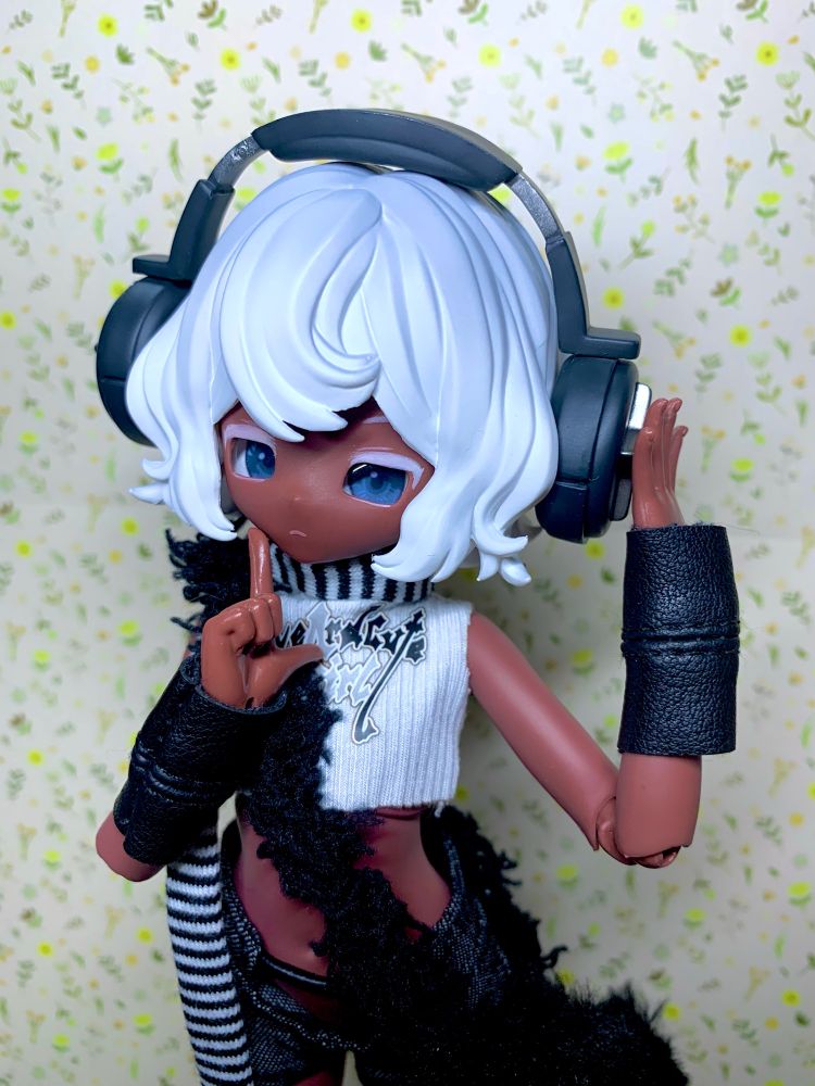 ブラインドドールの「変な少女」シリーズ、一番星の写真です。
褐色の肌に白い髪の毛、パンクな格好をしています。
右手を口に当て、左手をヘッドフォンに当てたポーズをしています。