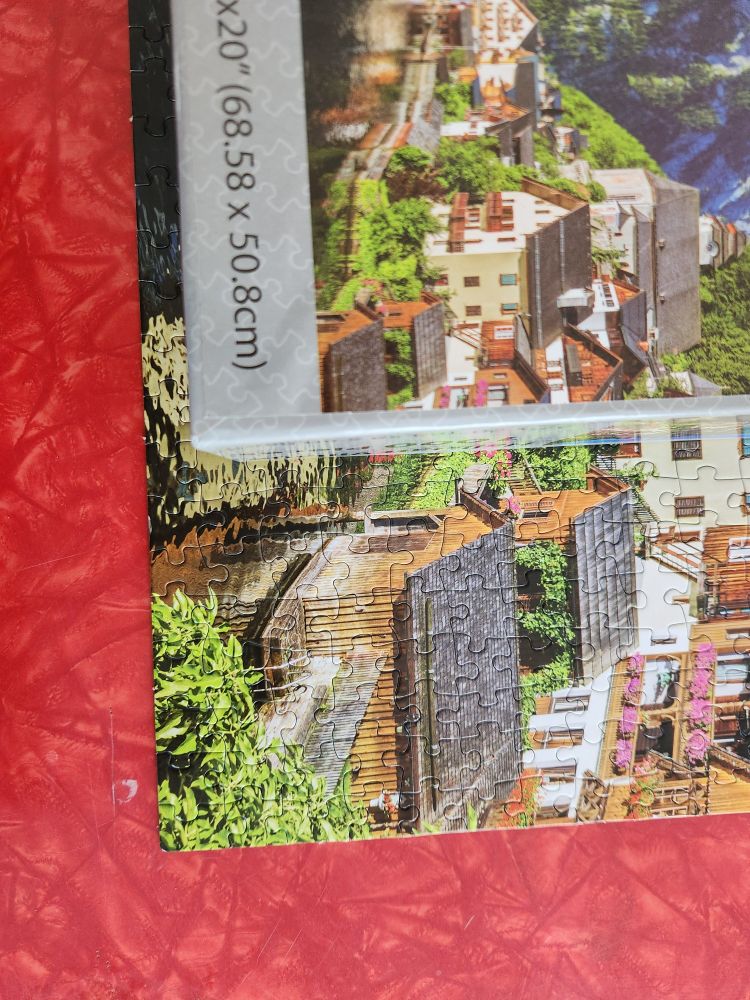 A picture of a completed corner of a puzzle with the puzzle box reference on top of the puzzle. The puzzle reference is cropped badly, making it look like the edge pieces should be different than what they actually are.