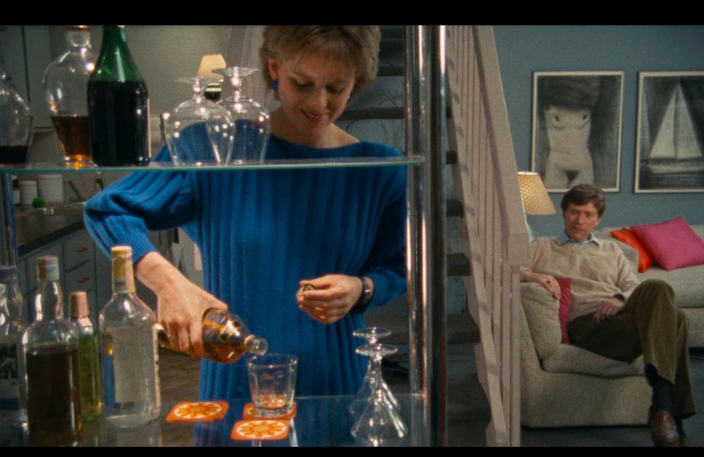 Plan du film. Le personnage principal, a gauche, sert un verre à un client, à droite. Le personnage principal, entre les barres du bar, semble enfermé 