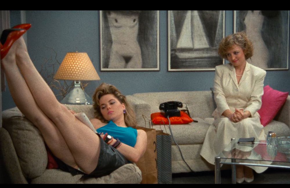 Une des travailleuses du sexe, à gauche, les pieds avec ses chaussures à talons rouges adossés contre le mur. Et la patronne, à droite, la regarde d’un air sévère et infantilisant