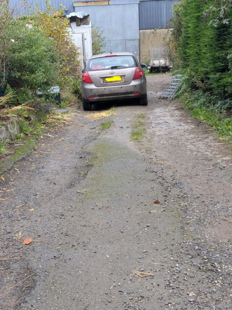 A rutted lane with farm buildings at the end of it. A slightly battered old Kia Ceed is parked, which is a smallish hatchback car.