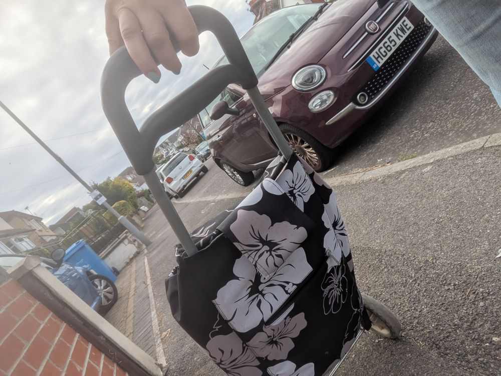 A black and white flower printed wheeled shopping trolley being pulled along a pavement.