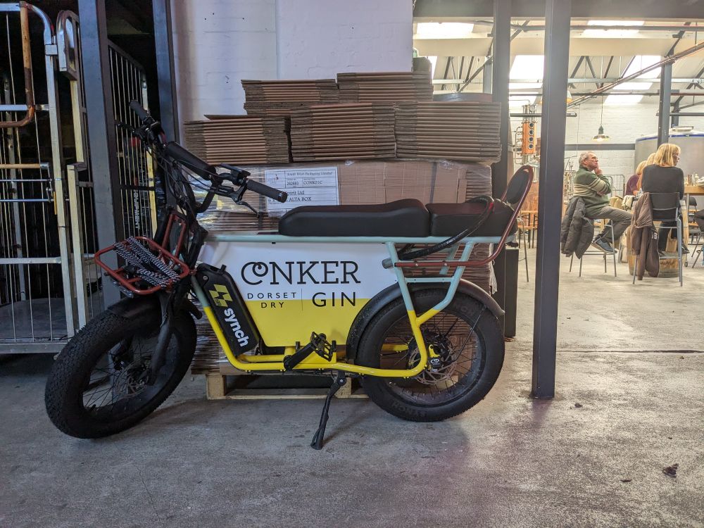 A Conker gin branded bike with fat wheels in a warehouse with people in the background sitting around having a G&T